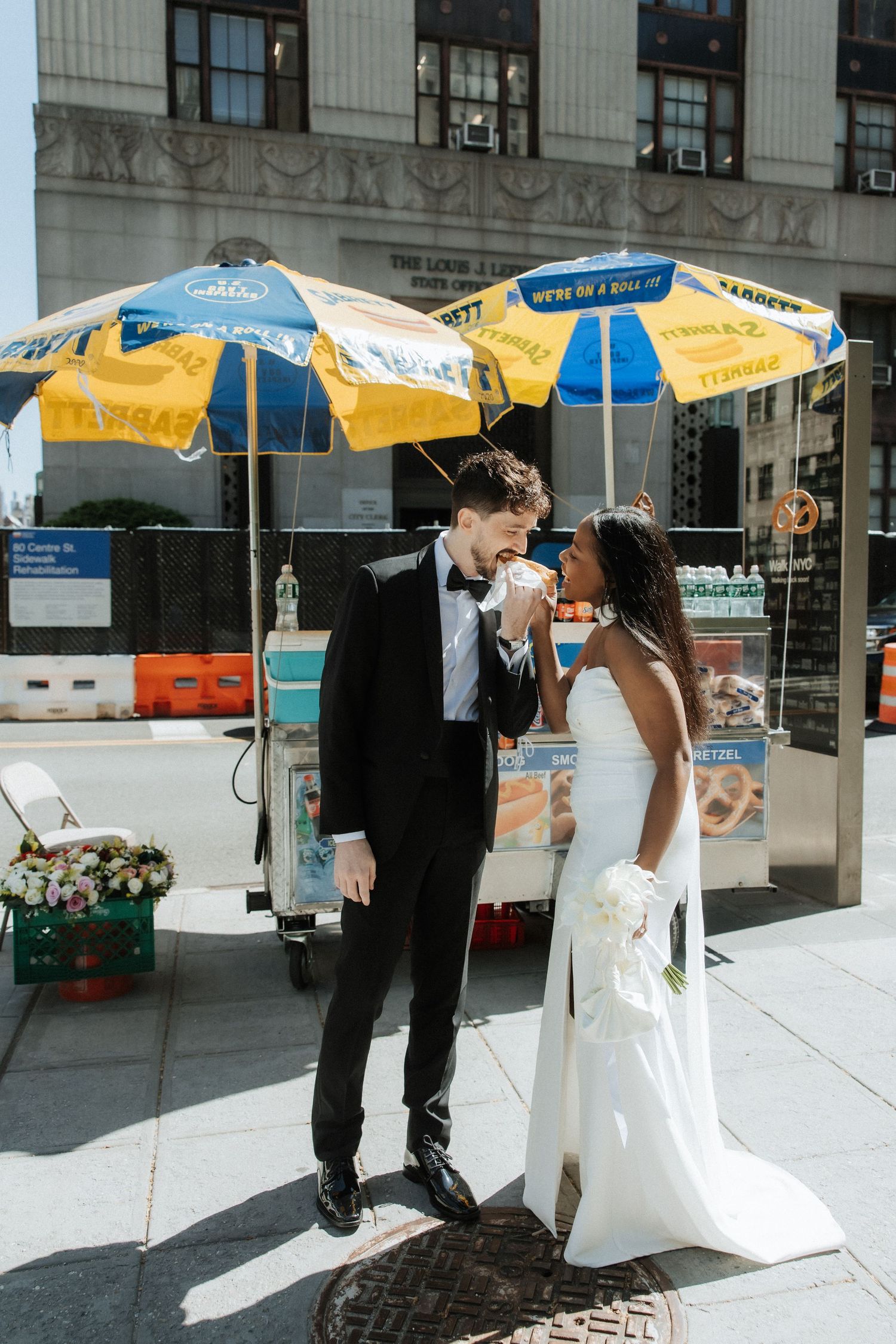 A wedding couple sharing a moment on a city sidewalk with yellow umbrellas in the background.