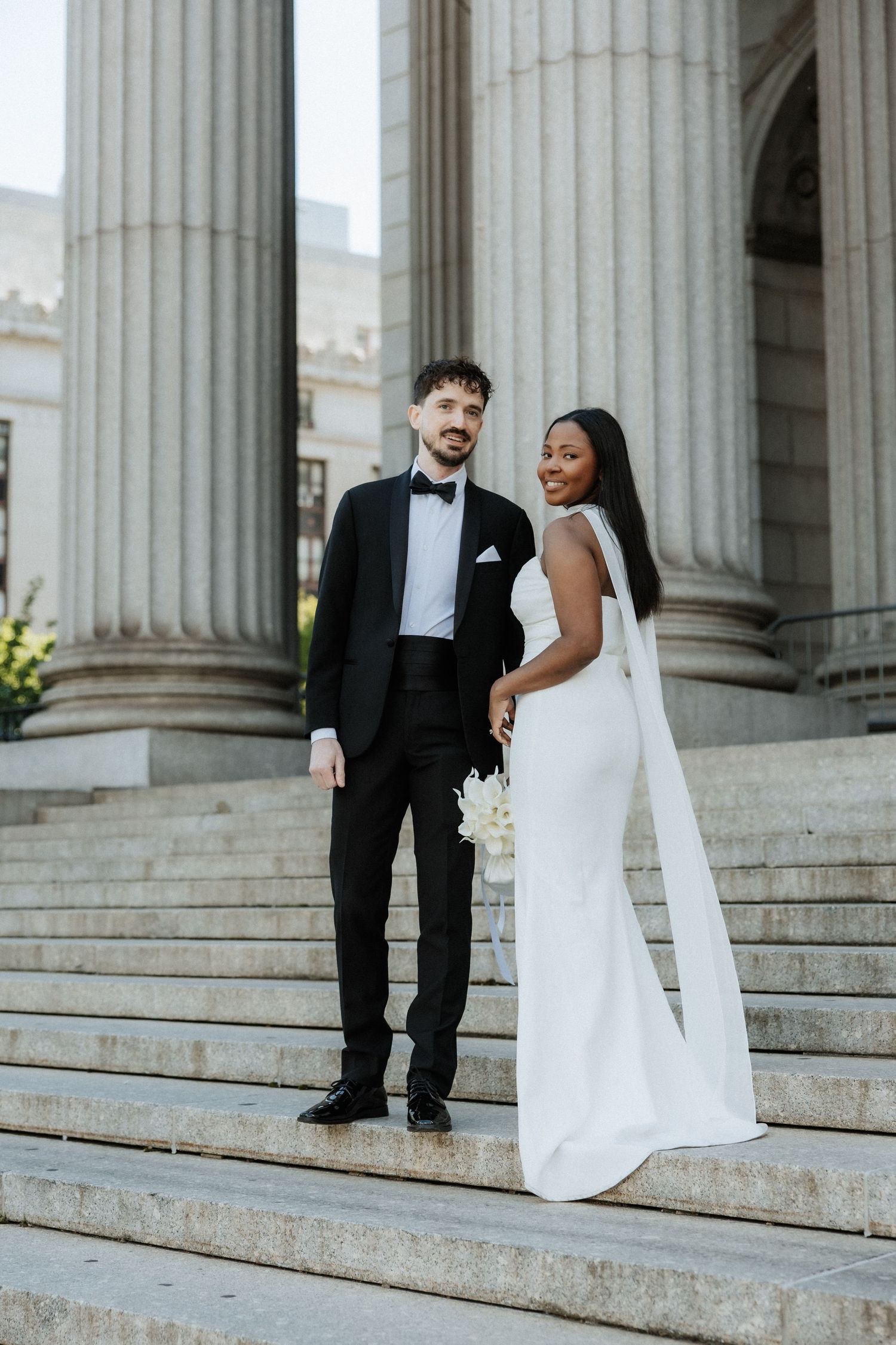 Wedding couple poses on grand stone steps with classical columns in the background.