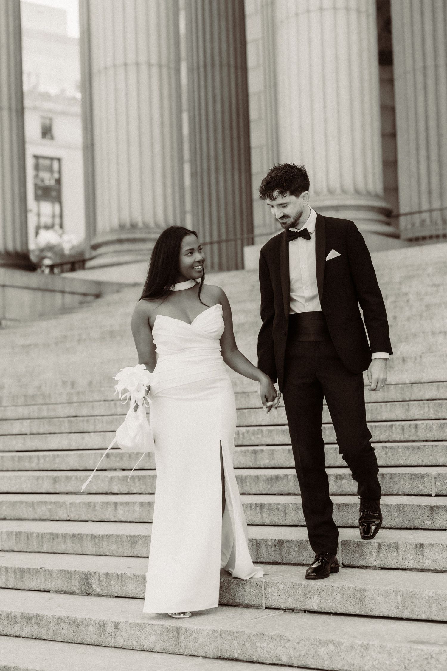 Black and white portrait of newlyweds on architectural steps with elegant columns.