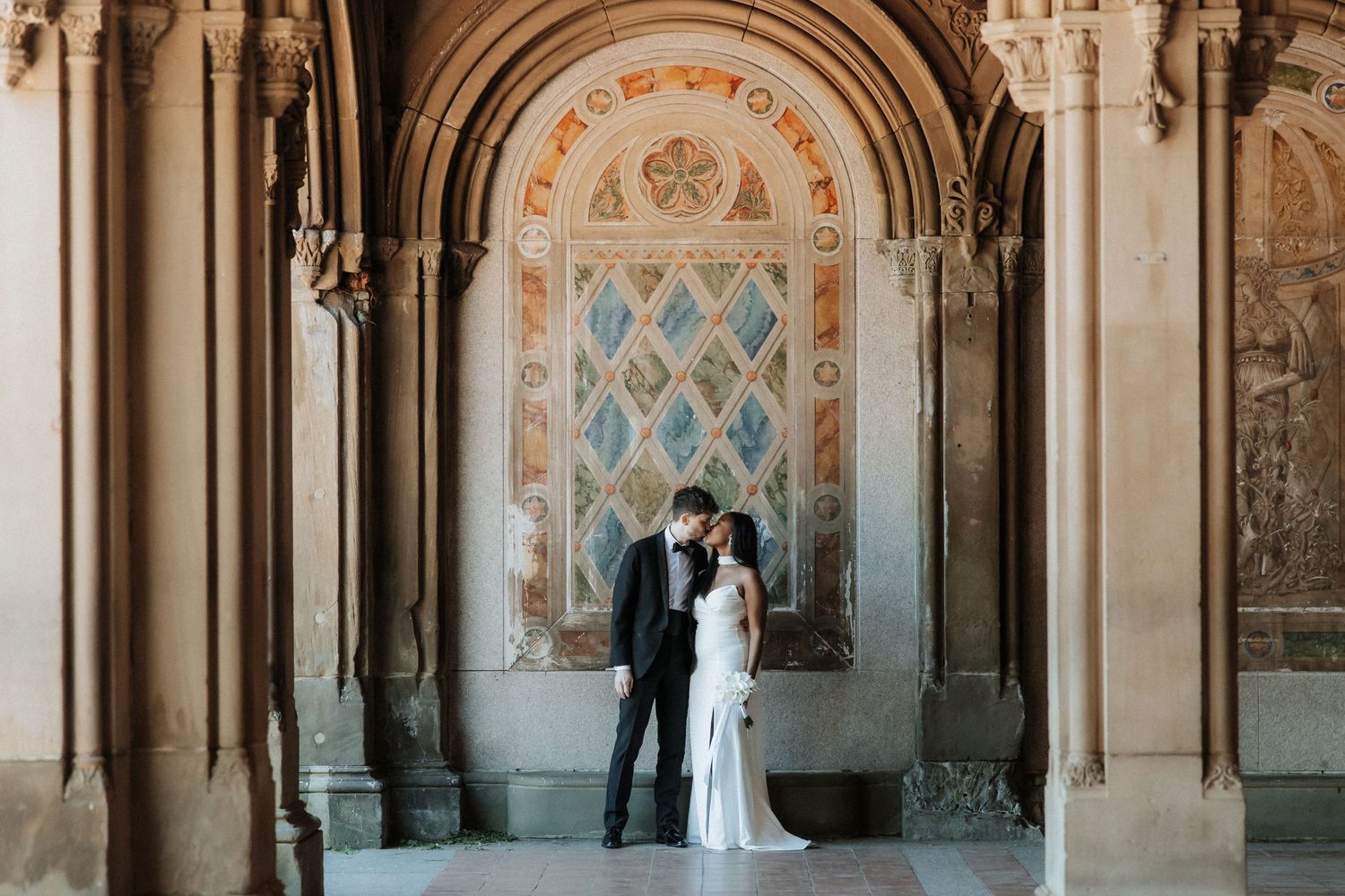 Romantic moment captured under ornate archway with beautiful architectural details.