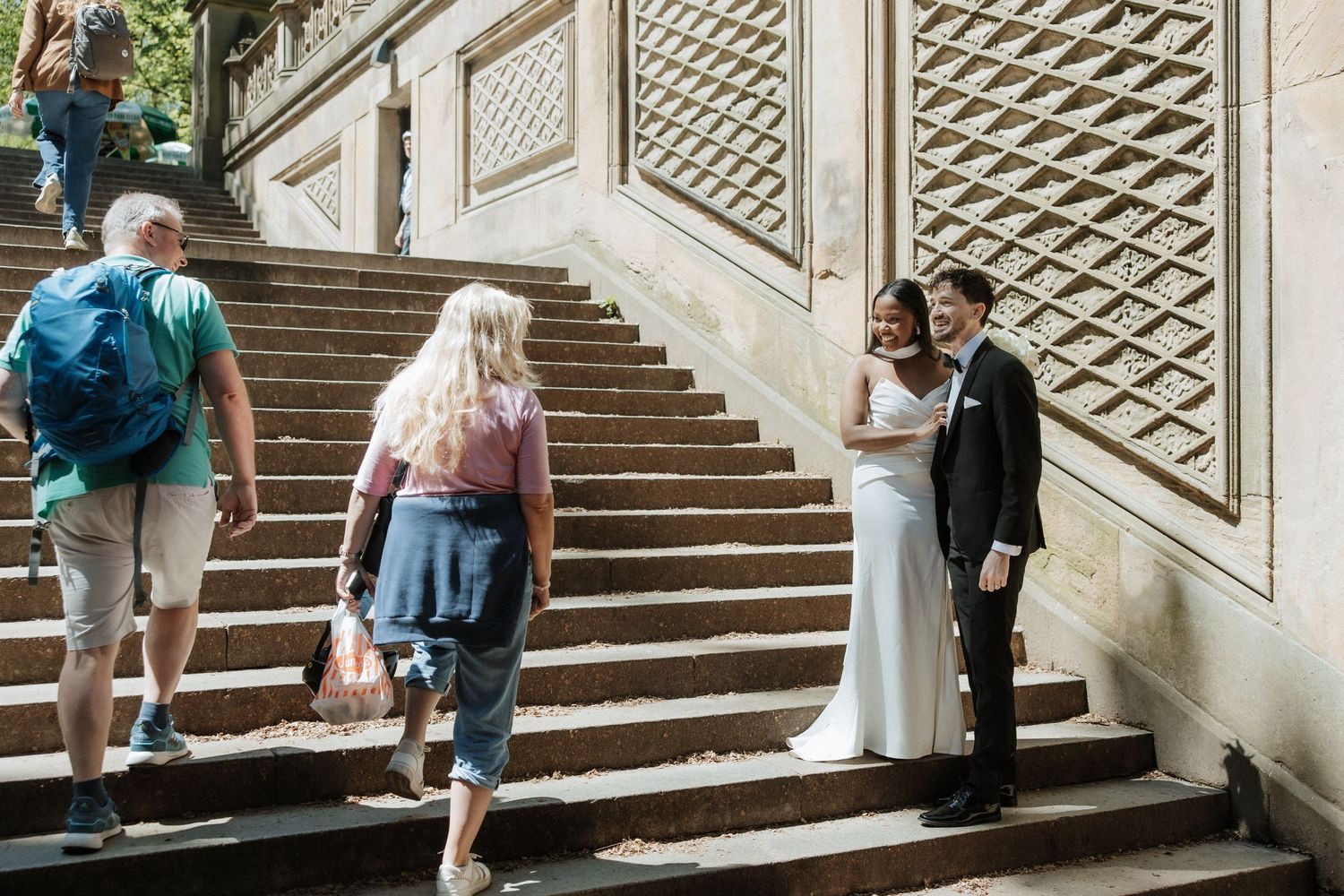 Wedding guests observe the couple on ornate stone steps with decorative patterns.