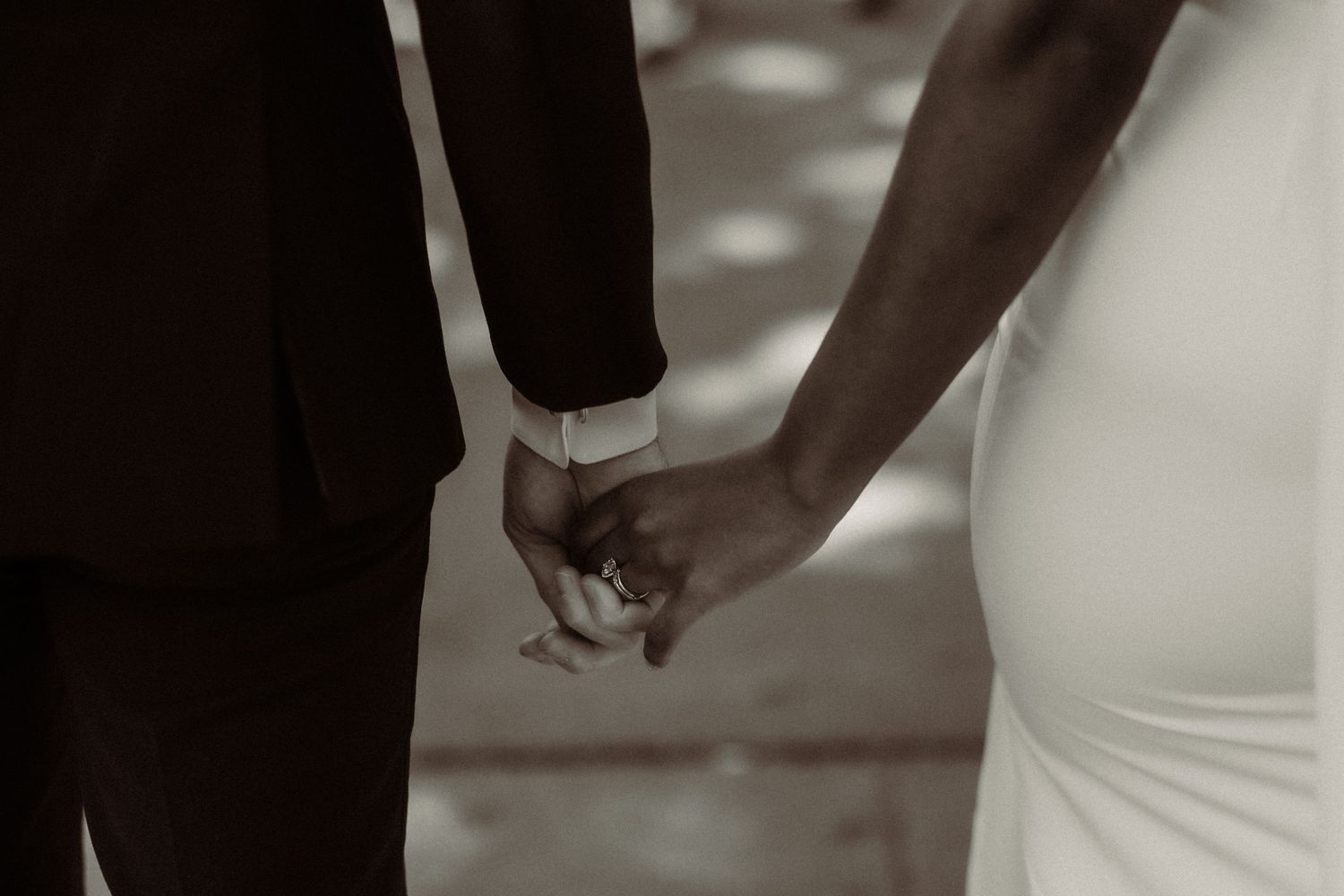 Intimate close-up of newlyweds holding hands in elegant wedding attire.