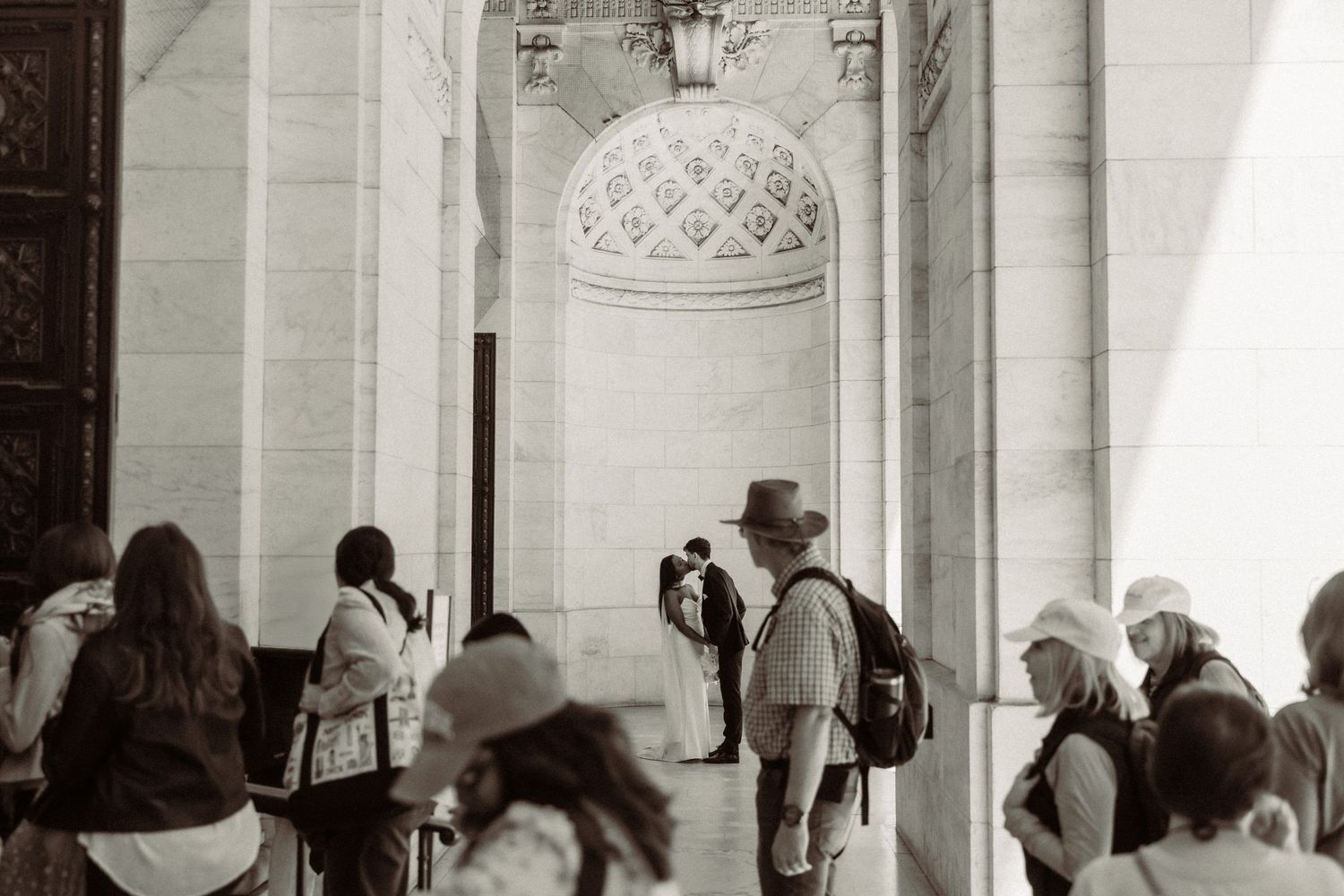 Wedding ceremony captured through crowd of onlookers at historic building entrance.