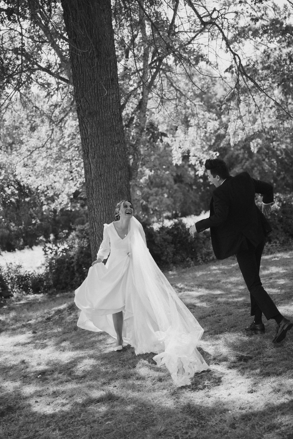 Bride in wedding dress sitting on ground surrounded by flowers in black and white photograph.