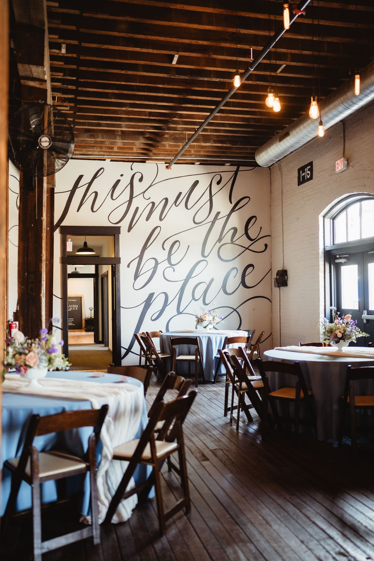 Rustic restaurant interior with wooden floors and a large decorative script text on the wall above dining tables.
