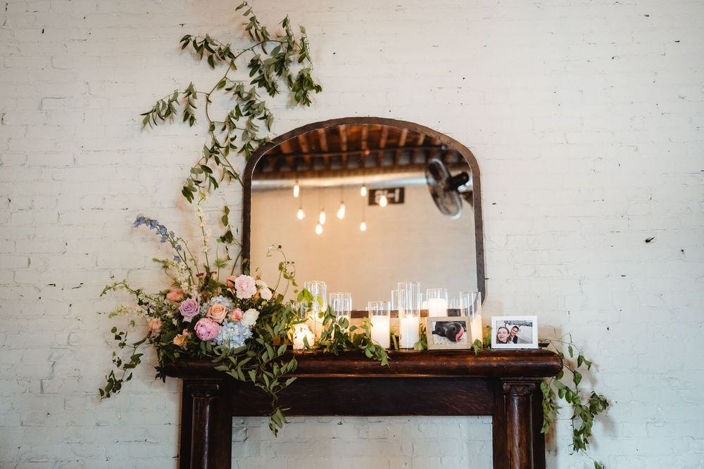 String lights and greenery decorate a rustic brick wall interior space with an arched doorway.