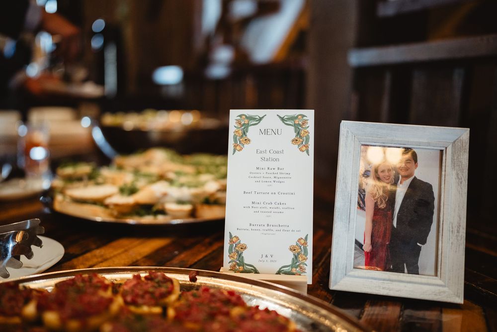 Wedding reception table with a menu card, framed photo, and several pizzas displayed on a rustic wooden surface.