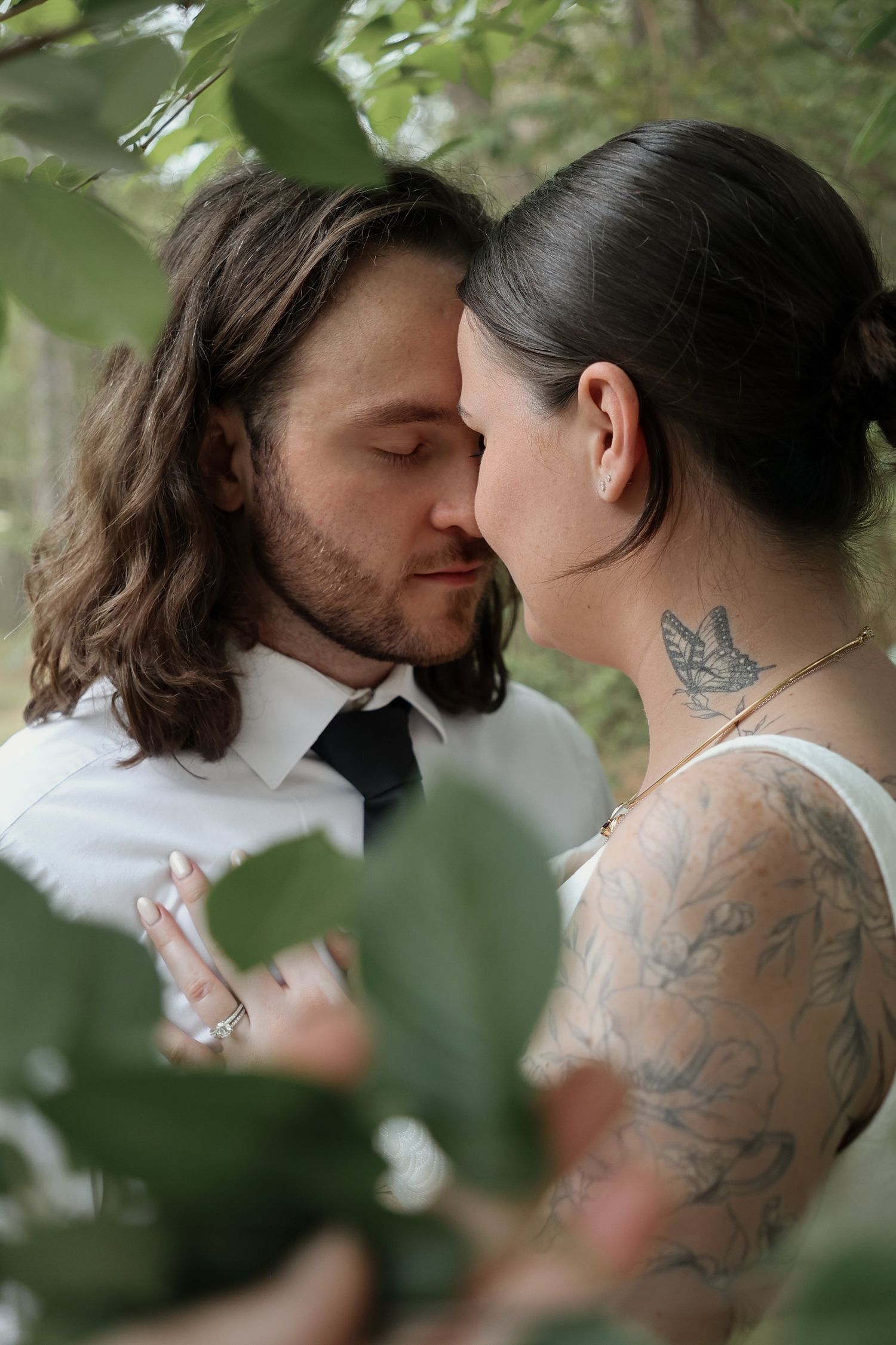 An intimate moment between newlyweds framed by green foliage.