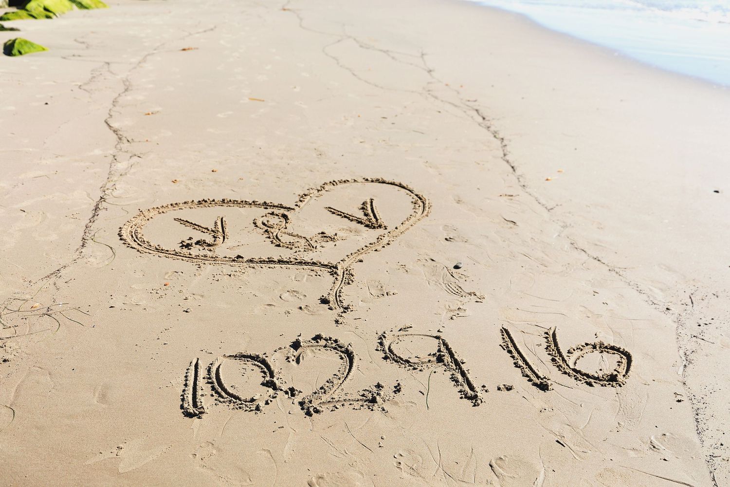 The word 'love' written in sand on a beach with heart symbol and arrow marking drawn above it.