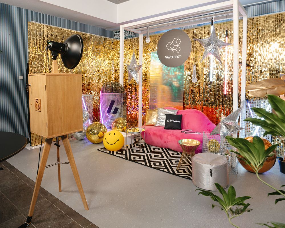 Vintage wooden photo booth beside glamorous gold sequin backdrop with colorful lounge seating.