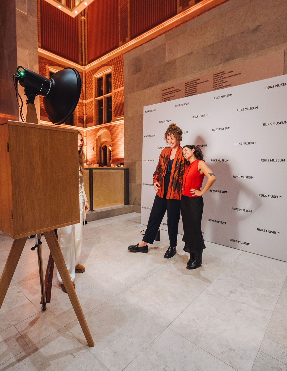 Two women posing before Rijks Museum step-and-repeat backdrop beside vintage wooden photo booth.