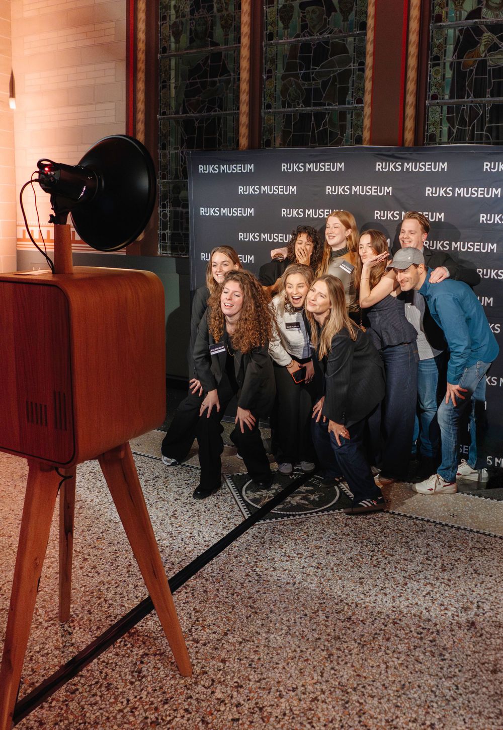 Group of people posing and laughing before Rijks Museum branded step-and-repeat photo booth backdrop.