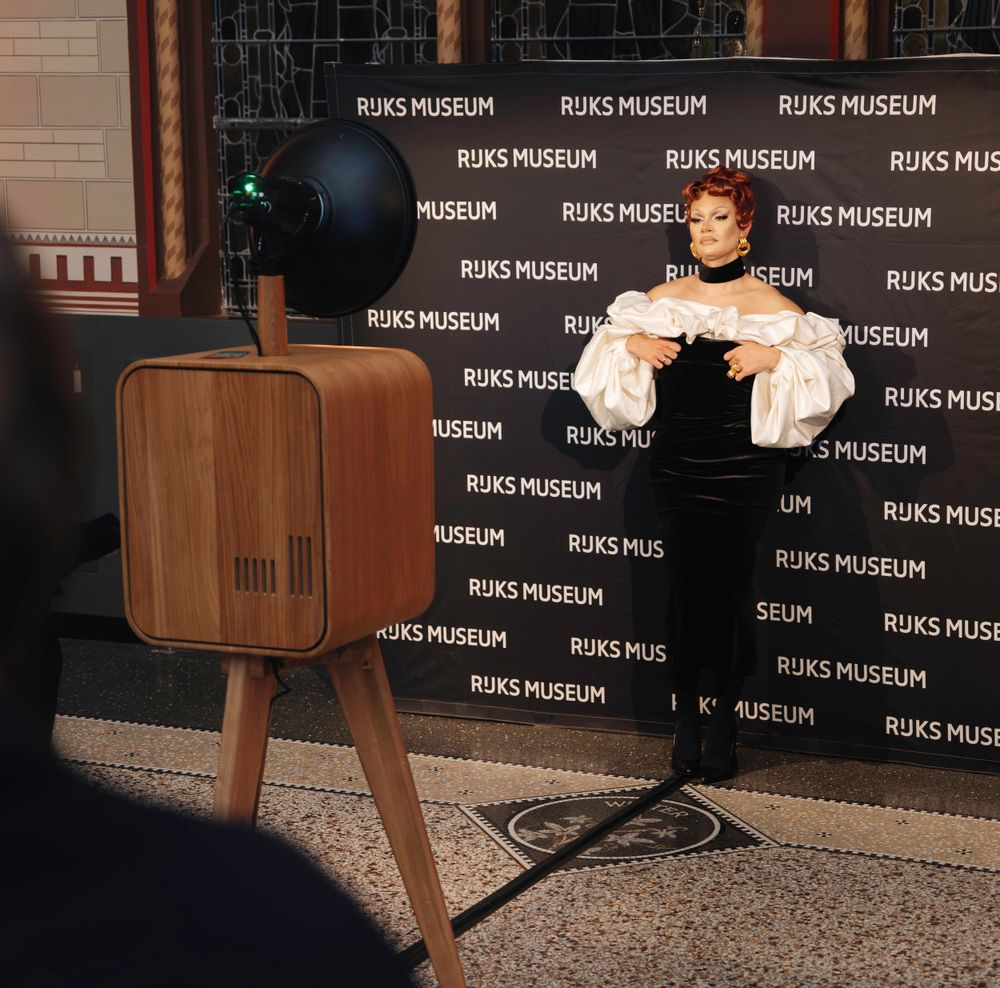 Elegant woman in white ruffled blouse posing at Rijks Museum branded photo booth backdrop.