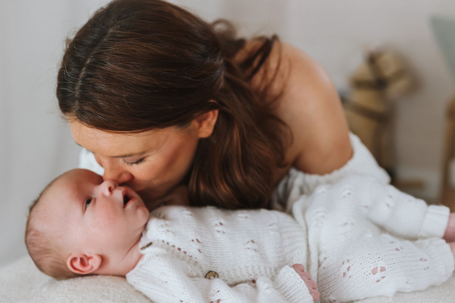 Baby wearing white knitted sleeveless romper lying on soft cream blanket.