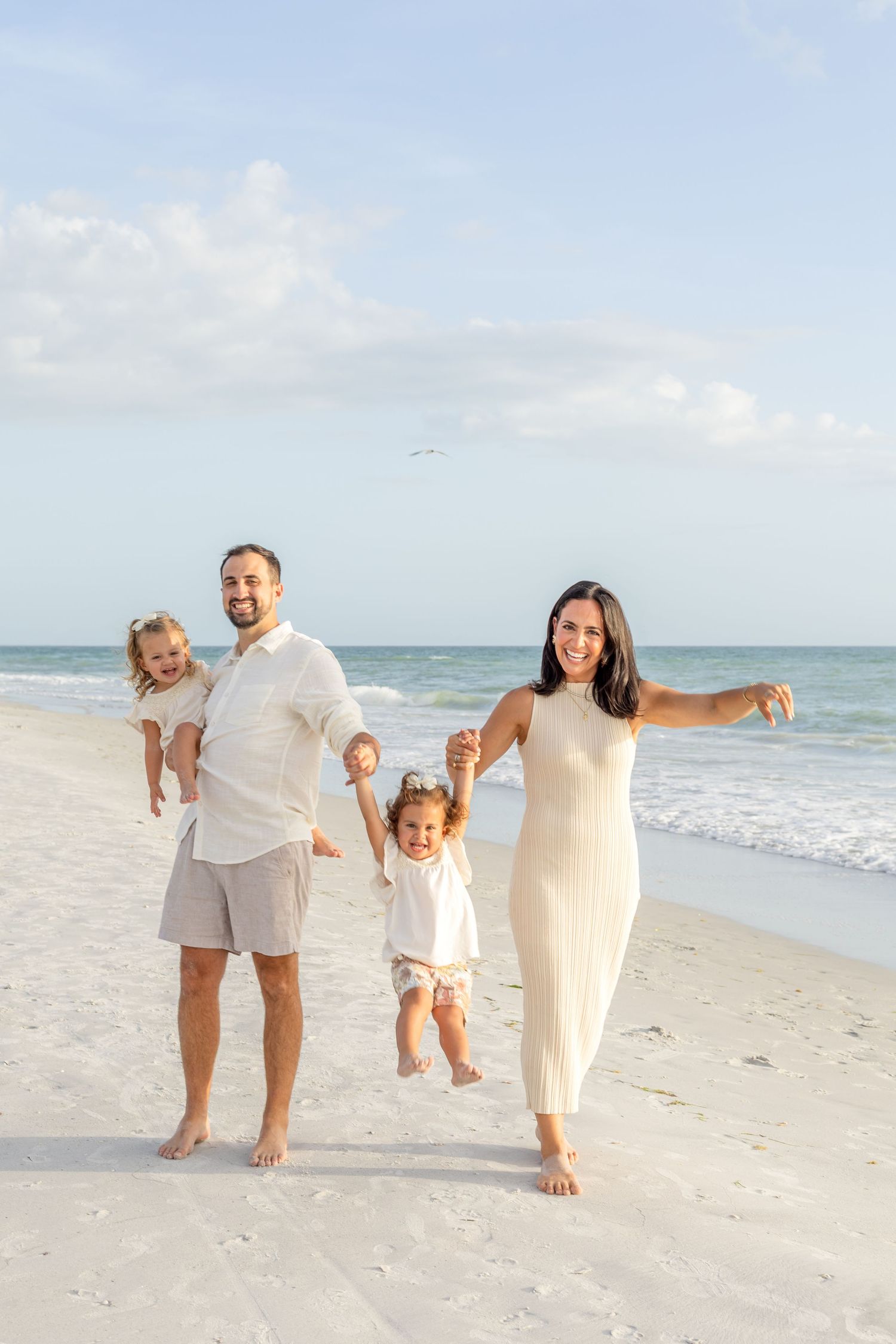 Joyful family of four playing on a sunny beach with two young children.