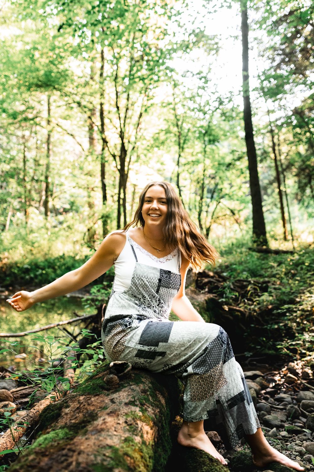Elegant forest portrait of a senior girl sitting on a fallen tree.
