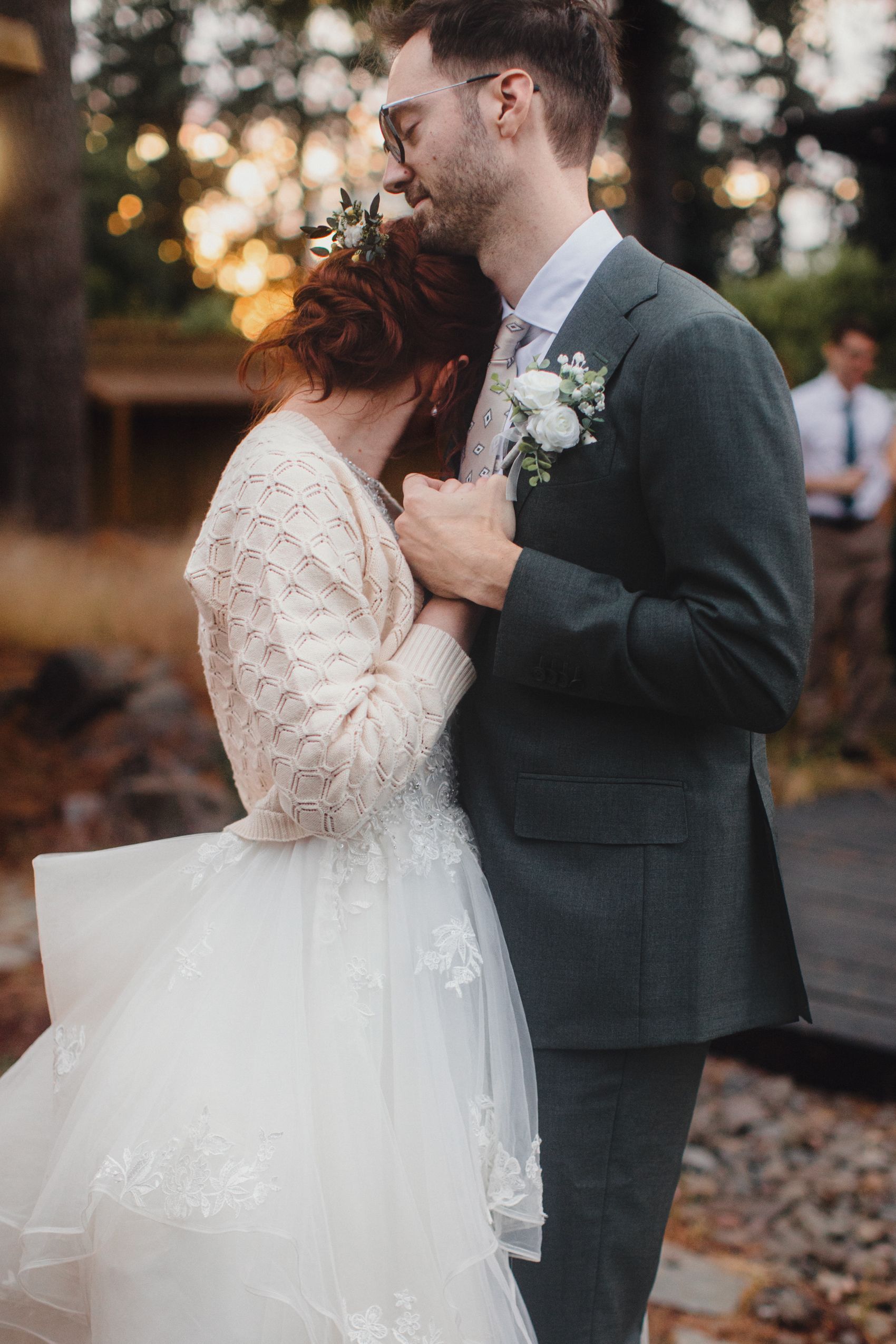 Romantic outdoor wedding moment at sunset with couple embracing in vintage-inspired lace gown and dark suit.