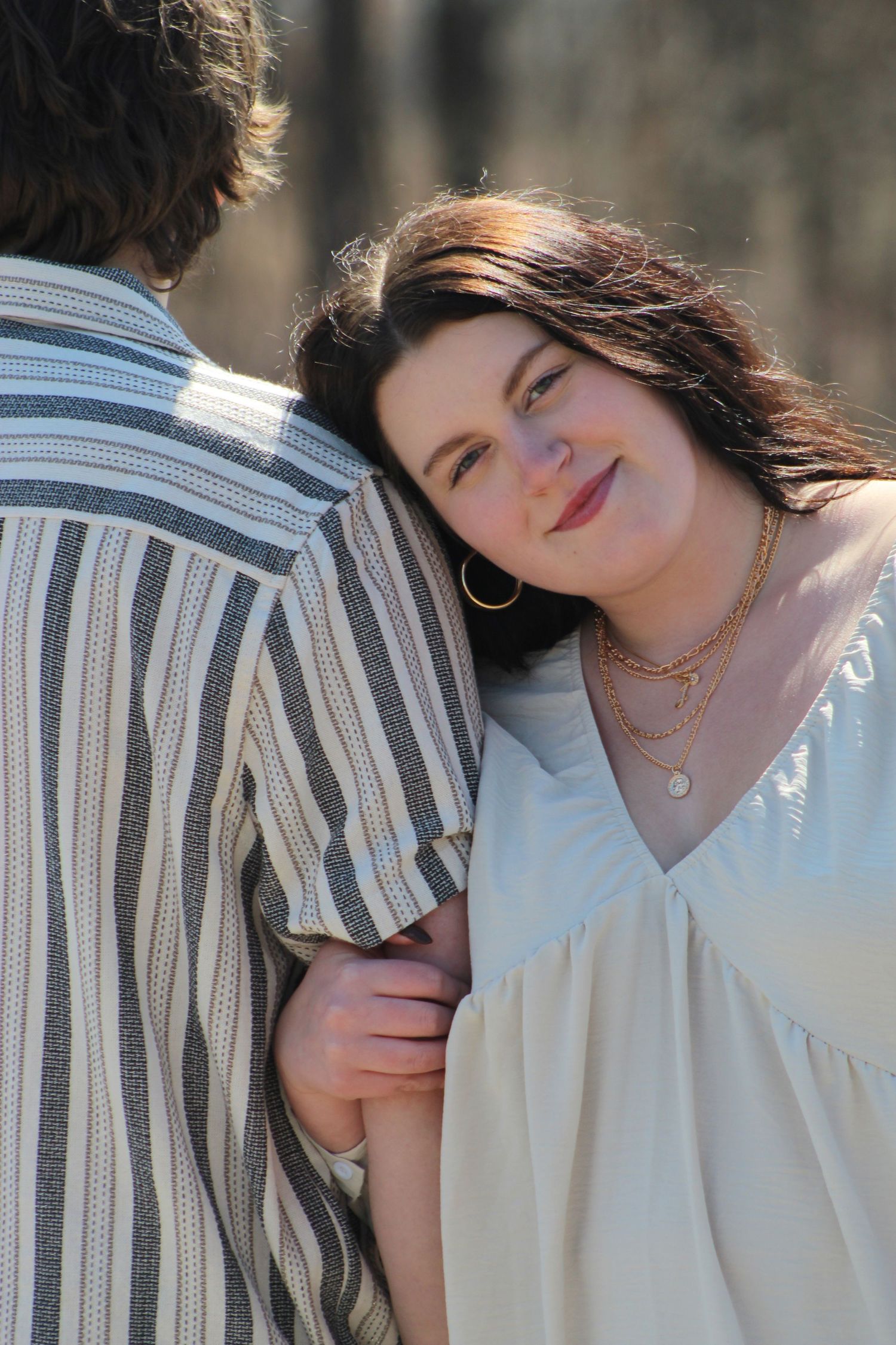 Intimate outdoor portrait showing tender romantic moment in sunlight with striped shirt and white dress.