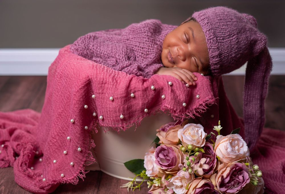 Newborn photography setup with baby posed on pink textured blanket with roses.