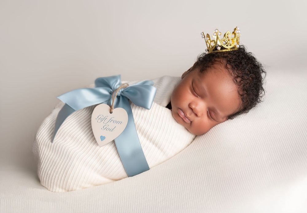 A newborn baby sleeping peacefully while wearing a white outfit with blue ribbon details.