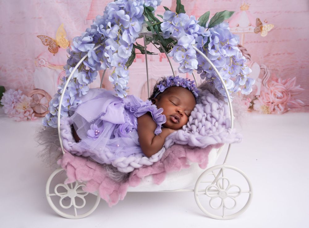 A sleeping baby lies on purple floral bedding in a dreamy pink-tinted nursery setting.