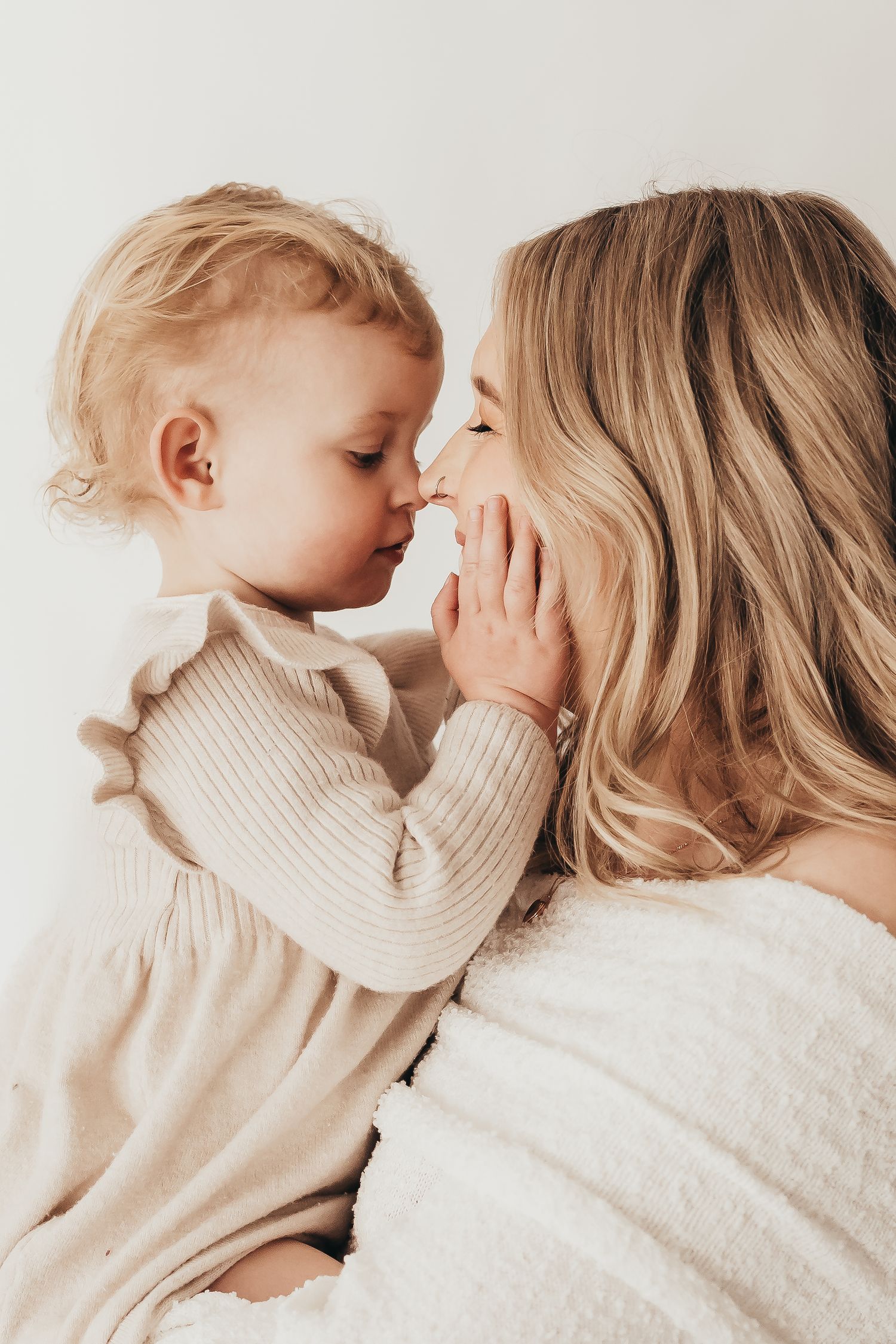 Intimate lifestyle portrait of parent and child in cream sweaters sharing tender moment.