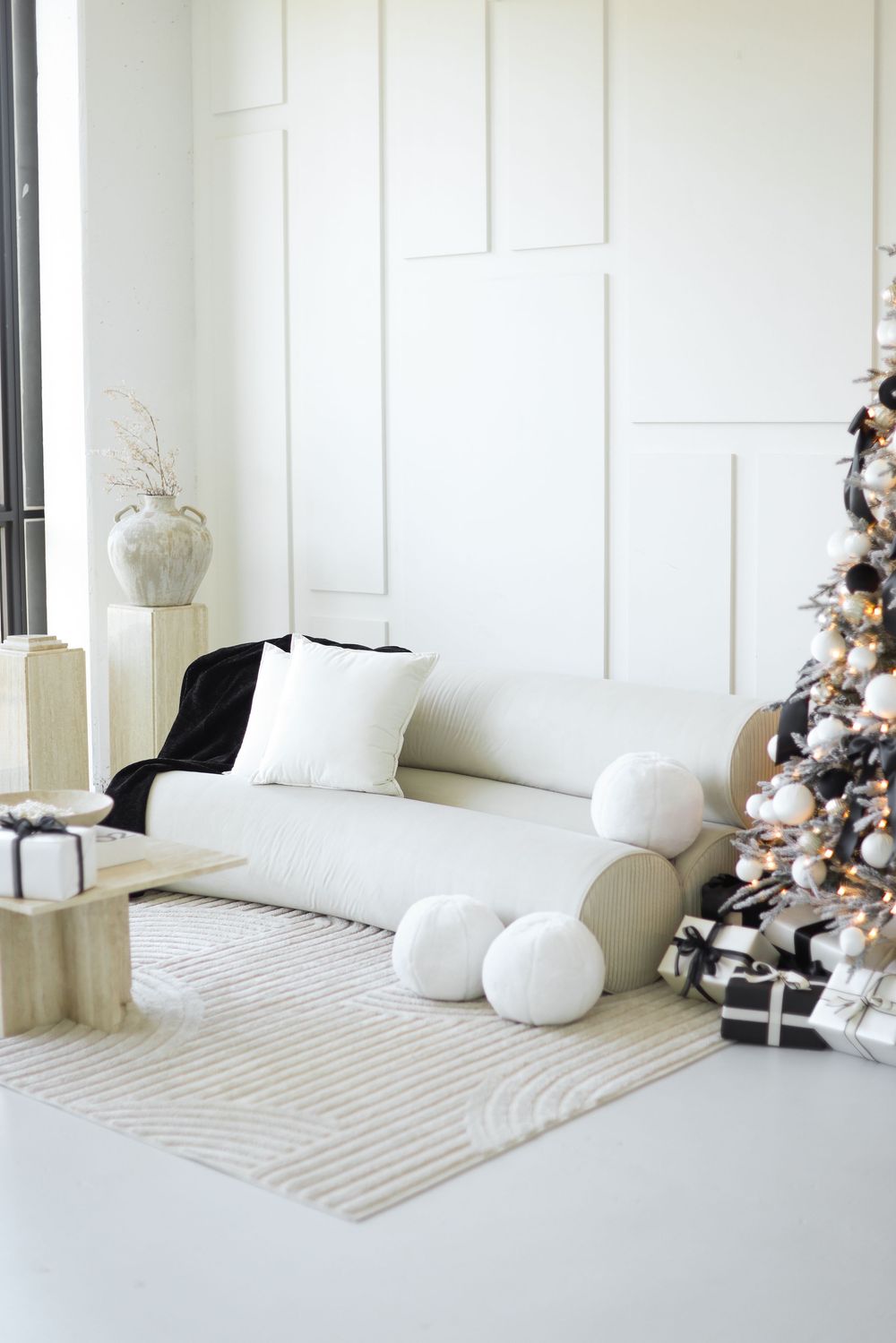 Modern minimalist living room with white couch, Christmas tree and wrapped presents in monochromatic white and black decor.