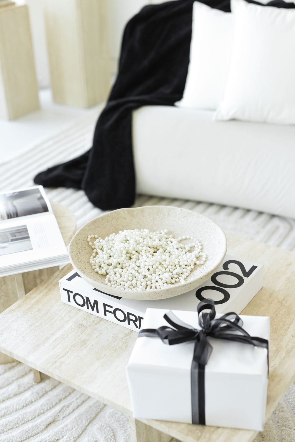 Cozy bedroom setting with Tom Ford book, white gift box with black ribbon, and popcorn bowl on white bedding.