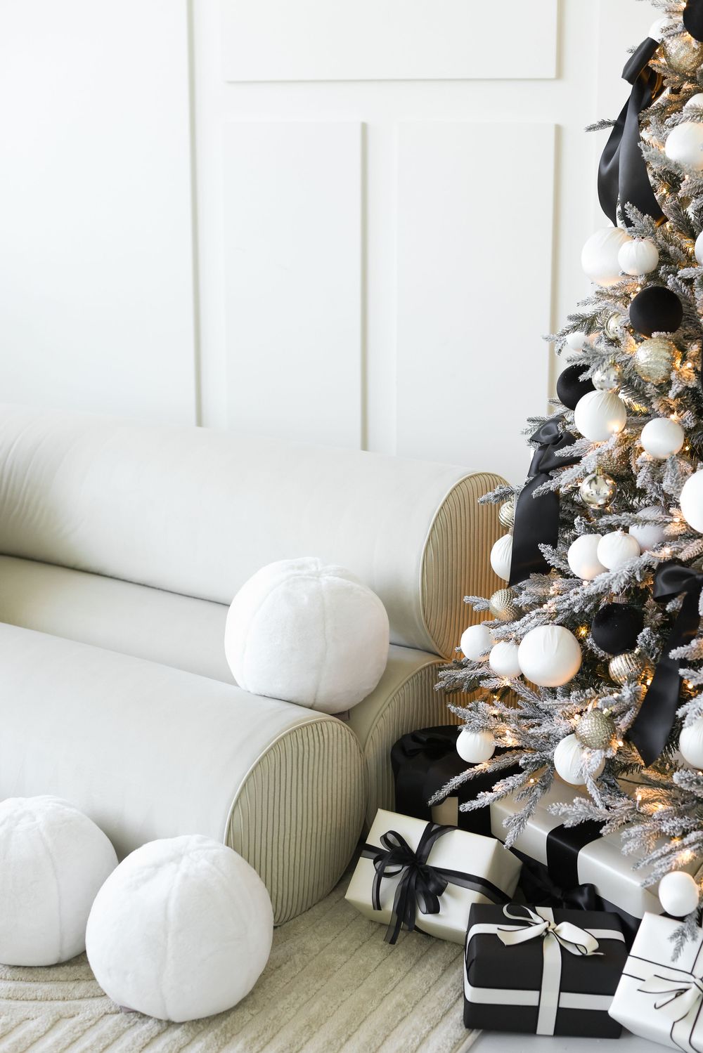 Modern black and white Christmas tree with wrapped presents and plush white pumpkins beside a cozy white couch.
