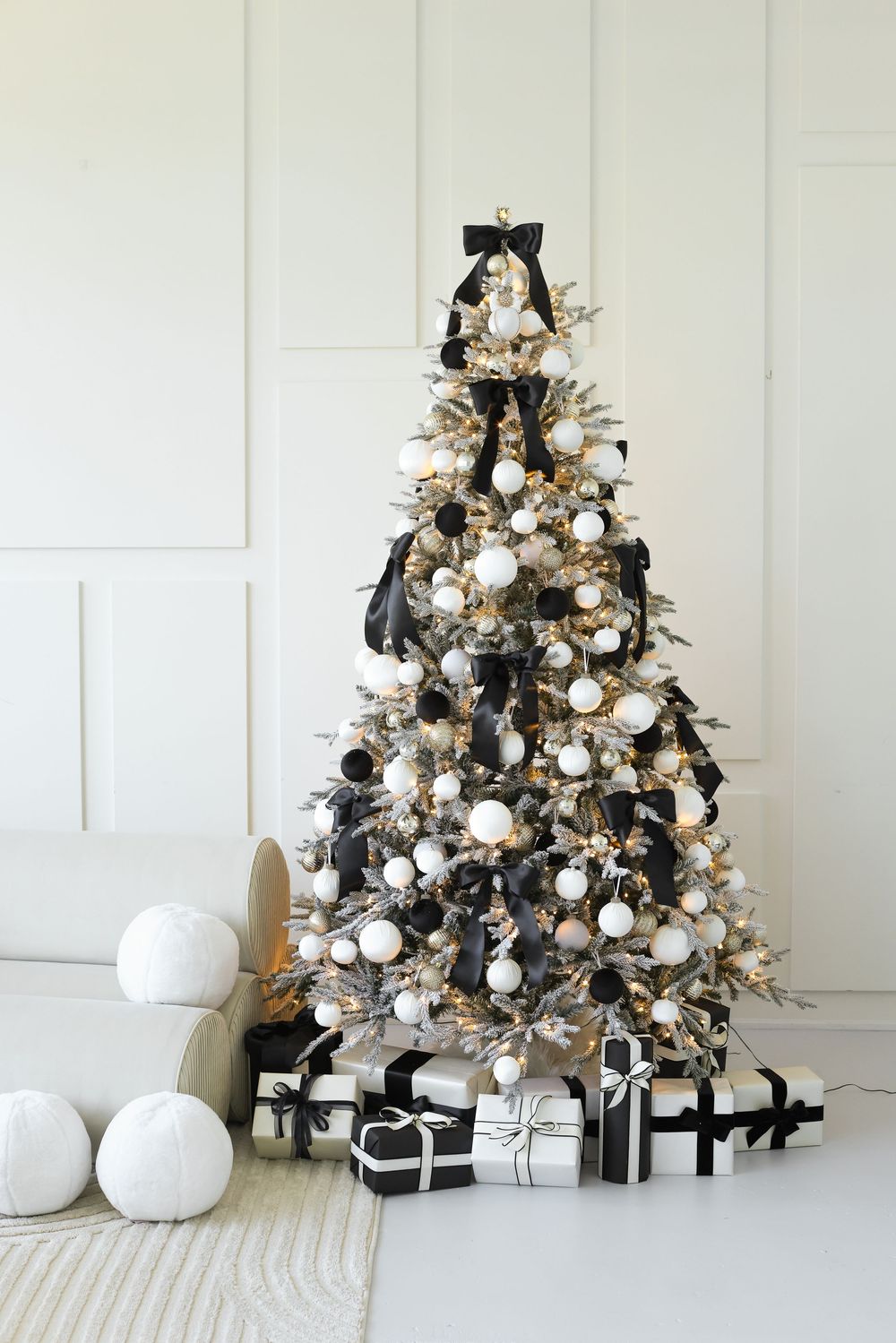 A white and black themed Christmas tree decorated with ornaments and presents showcases modern monochromatic holiday style.