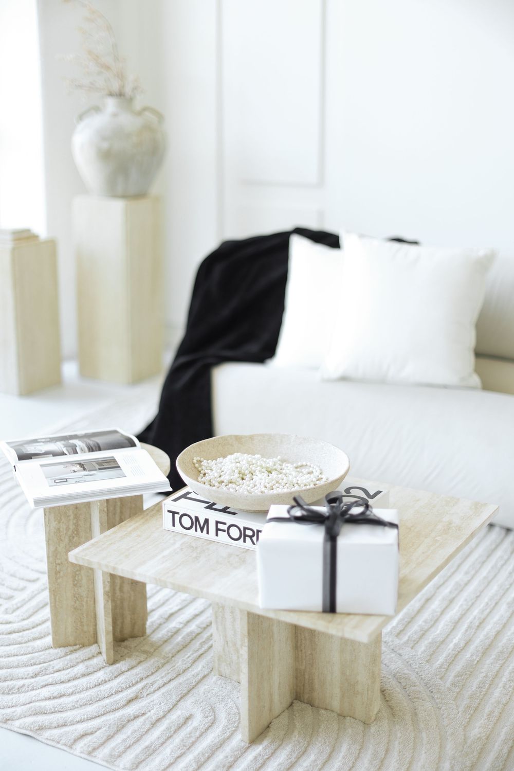 Modern minimalist living room with Tom Ford book, white gift box and decor on textured coffee table surface.