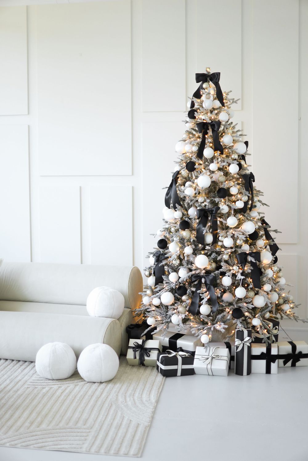 A black and white Christmas tree decorated with ornaments and snowballs sits against a bright white wall.