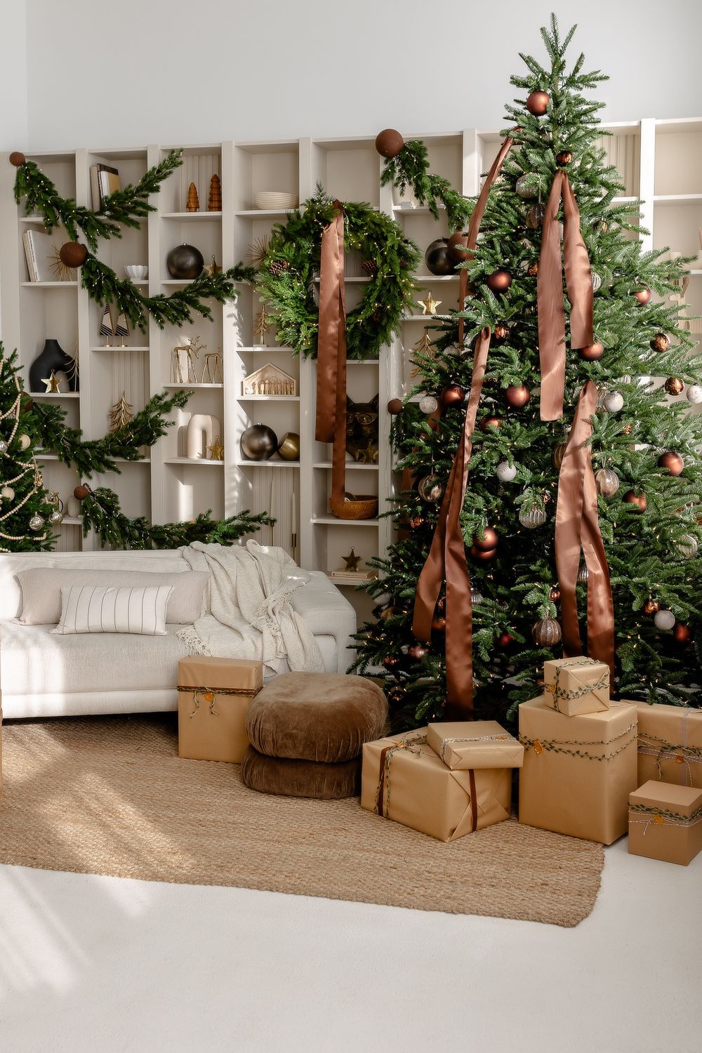 Modern Christmas living room with white shelving unit, decorated tree, brown ribbons and wrapped presents on jute rug.
