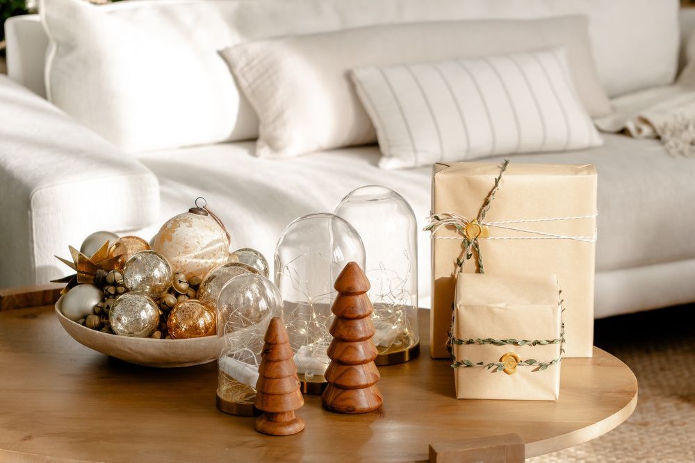 Cozy living room decor with wooden Christmas trees, glass domes, and ornaments arranged on a round coffee table.