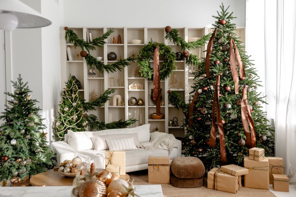 Modern living room decorated for Christmas with white furniture, wrapped presents, and multiple decorated trees.