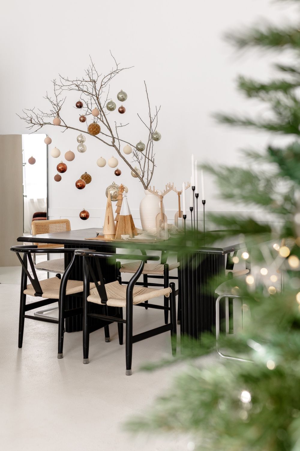 Modern Scandinavian dining room with black table, branch decor with copper ornaments, and partial Christmas tree view.