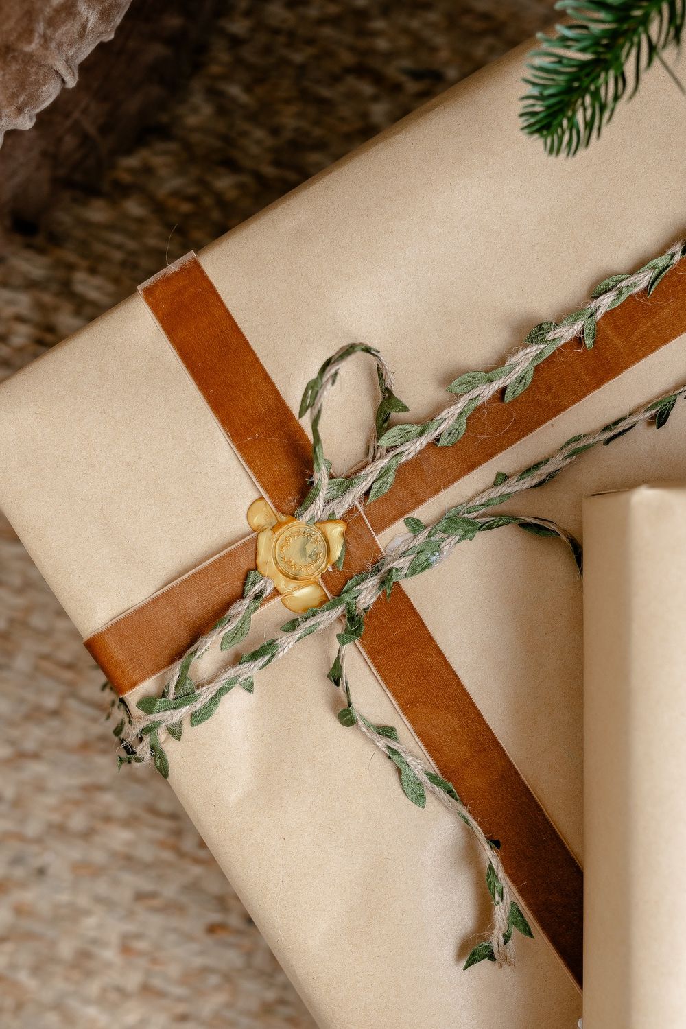 Artfully arranged gift wrapping featuring rustic brown leather ribbon intertwined with delicate green foliage on cream paper.