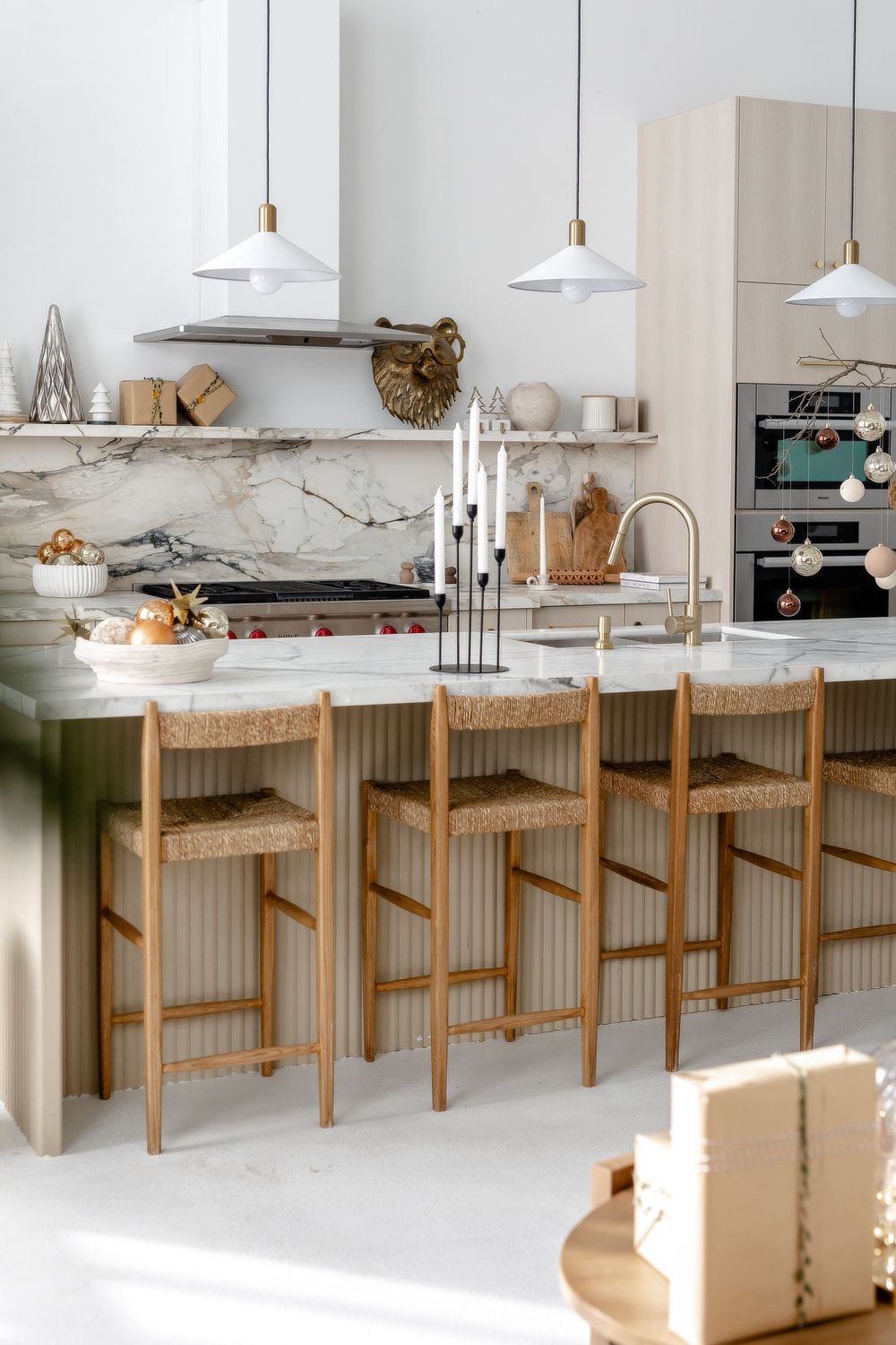 Modern kitchen with marble backsplash, white pendant lights, and wooden bar stools along a marble counter island.