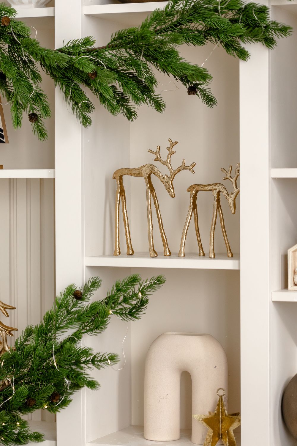 White built-in shelves decorated with evergreen garland, golden reindeer figurines, and ceramic vases for a modern Christmas look.