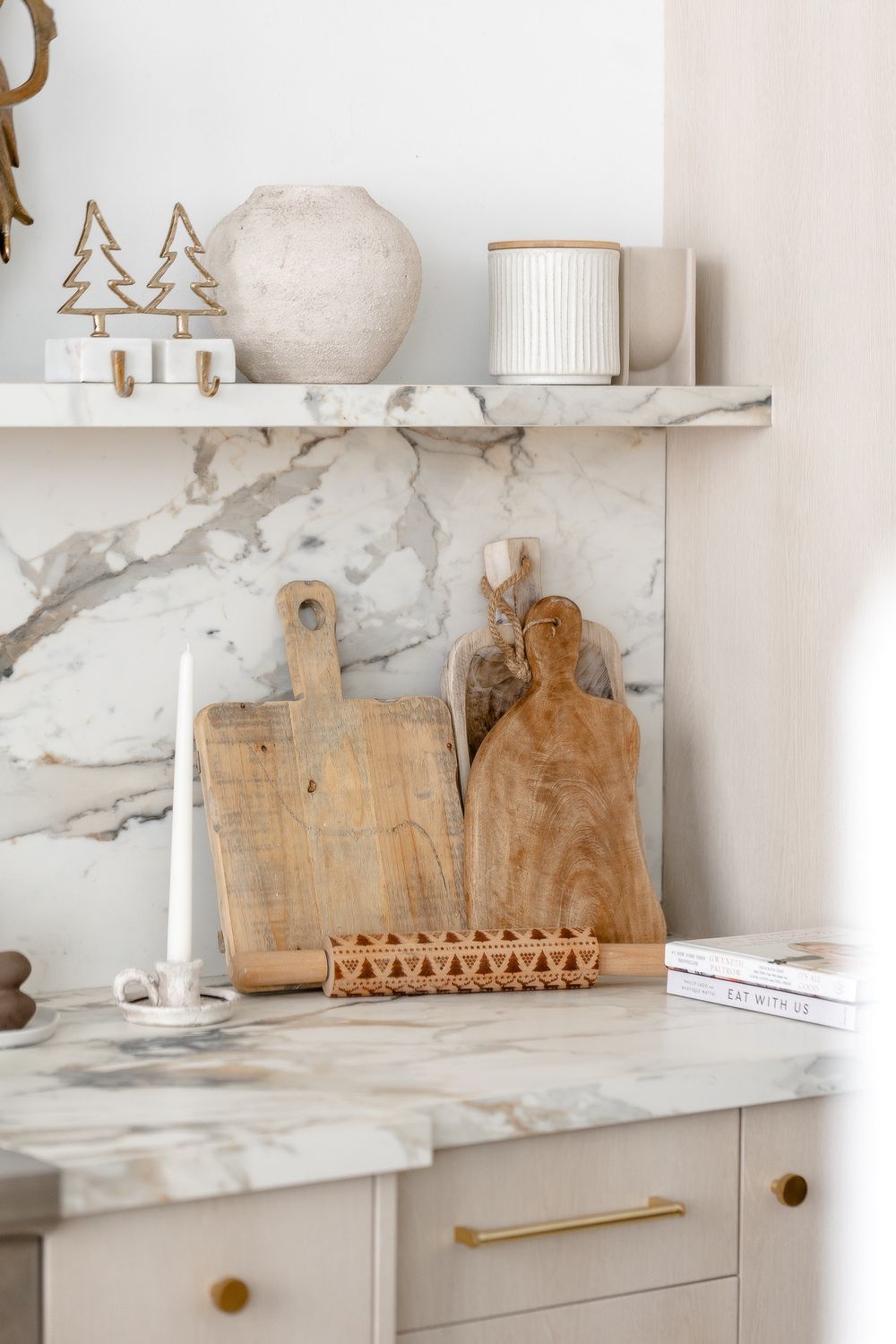 Modern kitchen corner with wooden cutting boards and marble backsplash displaying minimalist holiday decor on white shelving.