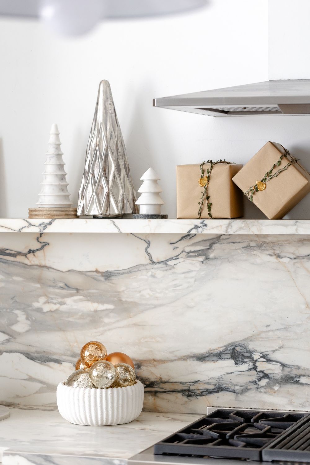Elegant kitchen shelf with decorative white trees, wrapped gifts, and marble backsplash featuring modern design elements.