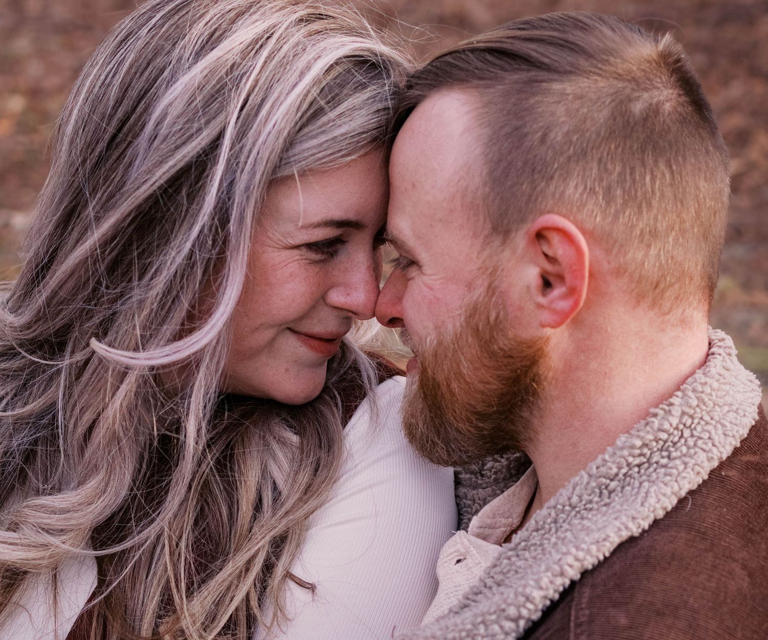 A tender romantic moment shared between a couple in cozy winter attire against a brick wall background.