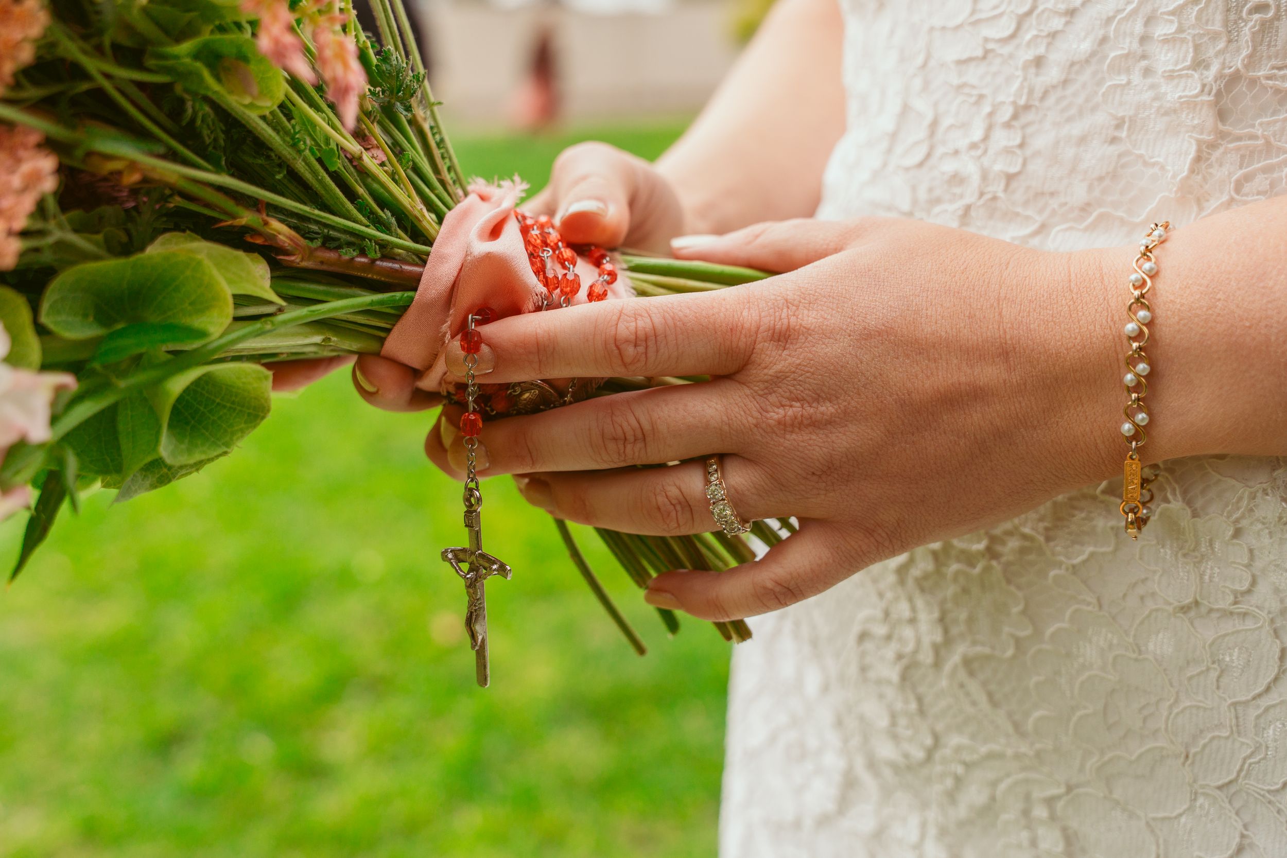 Close-up view of hands holding a bouquet of dark red calla lily flowers in natural outdoor setting.