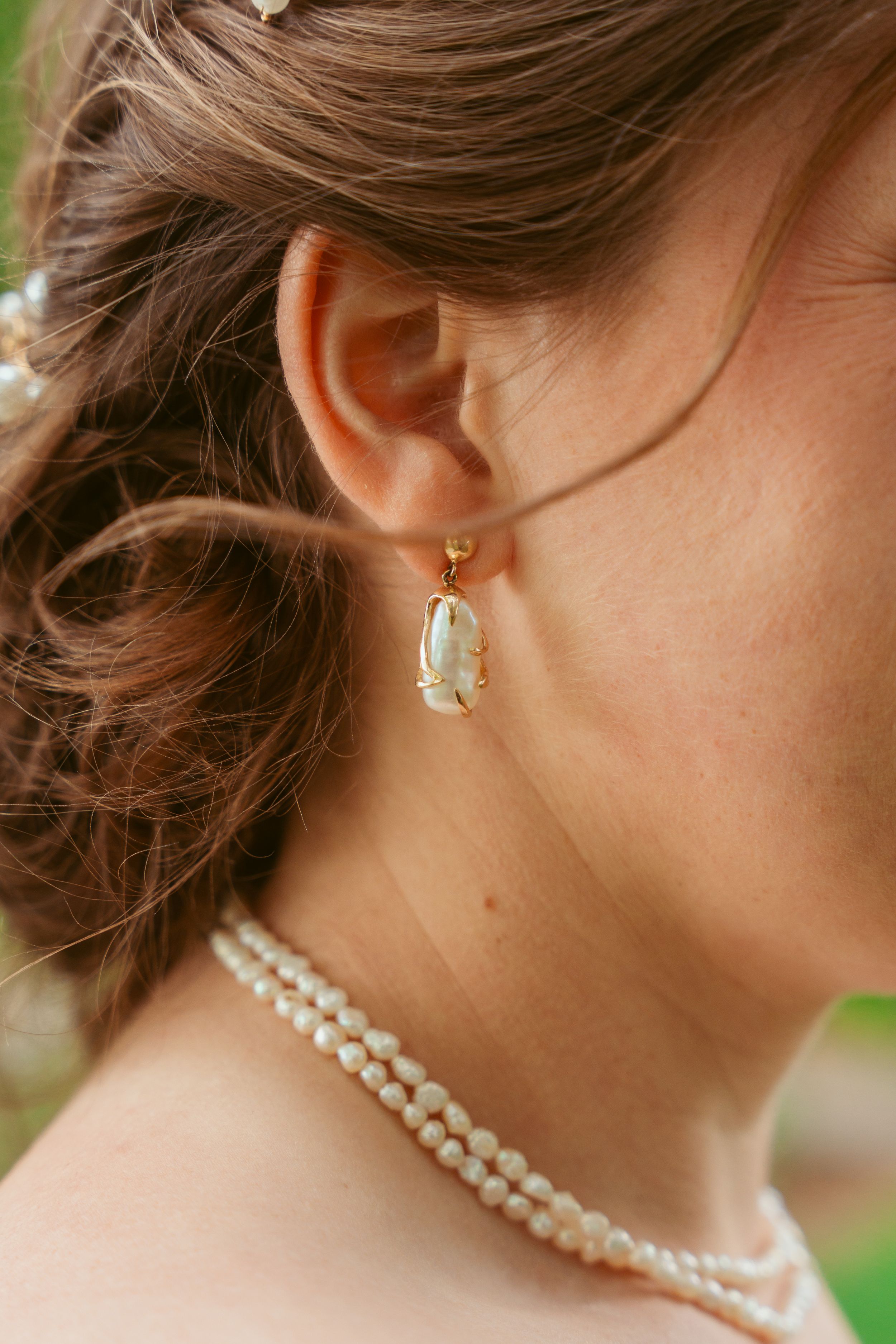 Close-up of an elegant pearl necklace and dangling crystal earring on woman wearing delicate jewelry.