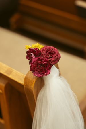 Deep burgundy dried rose decorates a church pew with flowing white tulle fabric for a wedding ceremony.