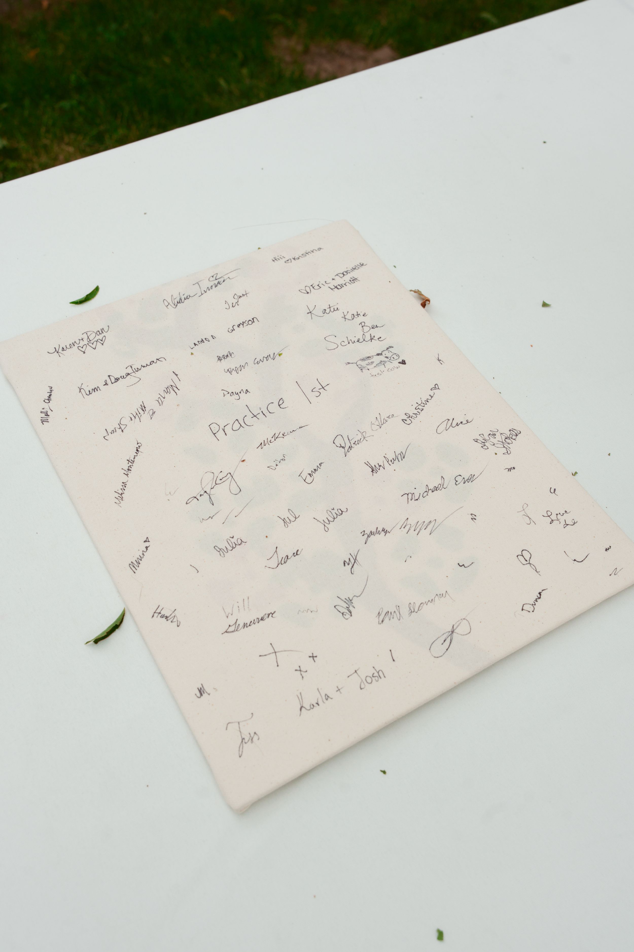 A white paper filled with multiple signatures and handwritten notes lies on a light surface with scattered green leaves.