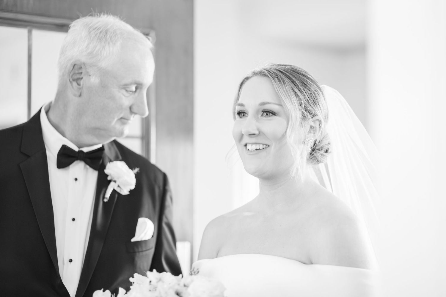 Black and white photo showing tender moment between father and daughter at wedding ceremony.