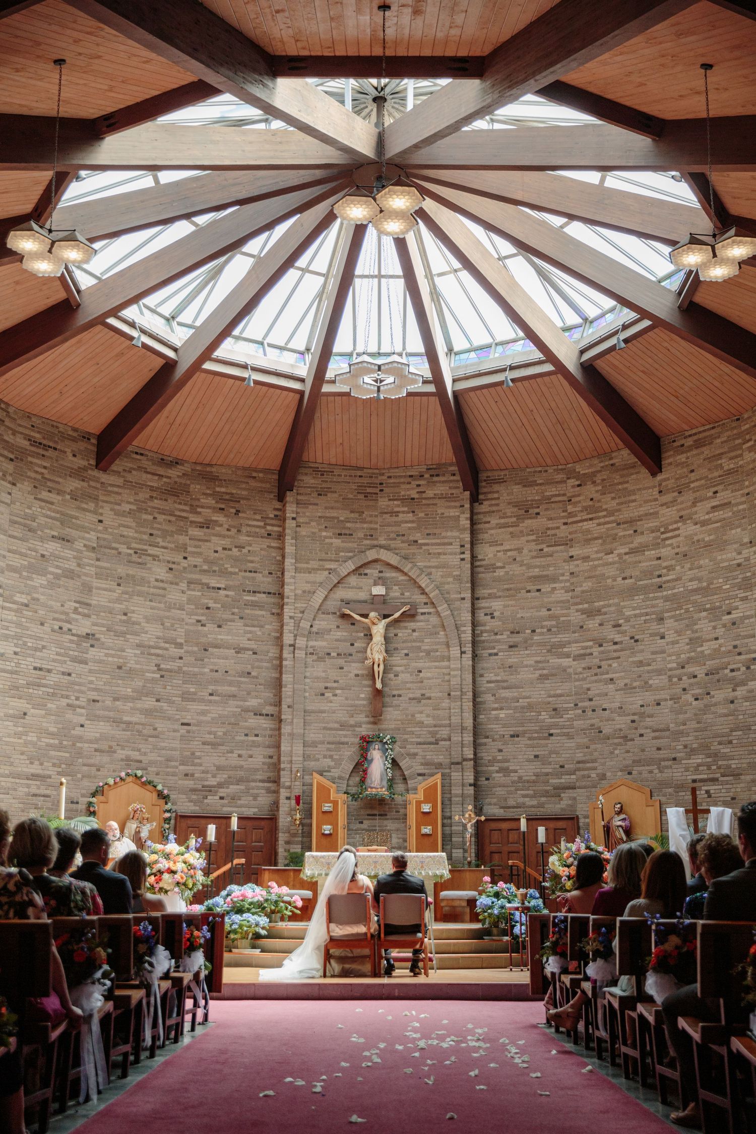 A modern church interior with octagonal skylight dome, stone walls, and red carpet leading to a crucifix altar.