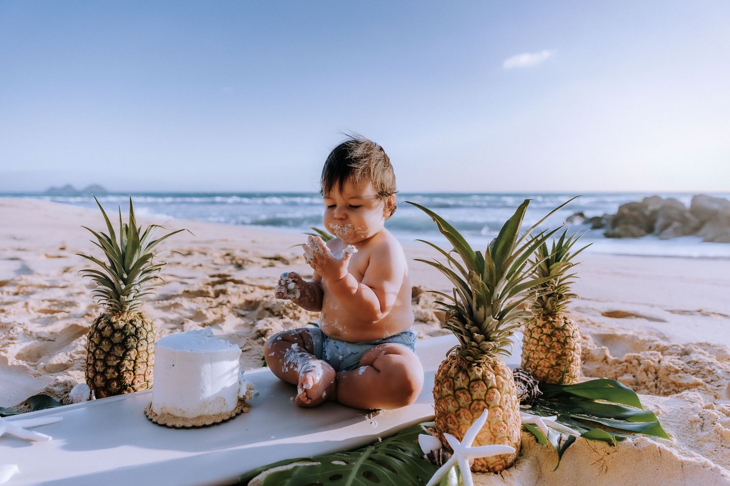 Tropical beach scene with pineapples and decorative elements arranged on sandy shore at sunset.