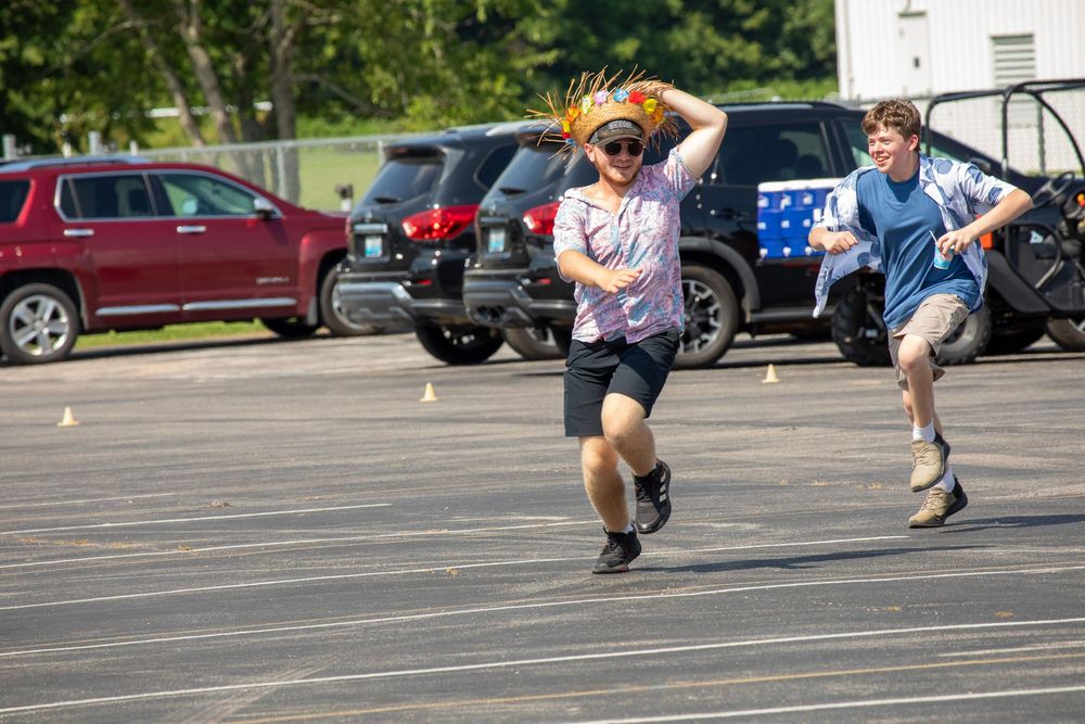 Two people compete in a high-intensity jump or leaping motion during an outdoor athletic activity in a parking lot.